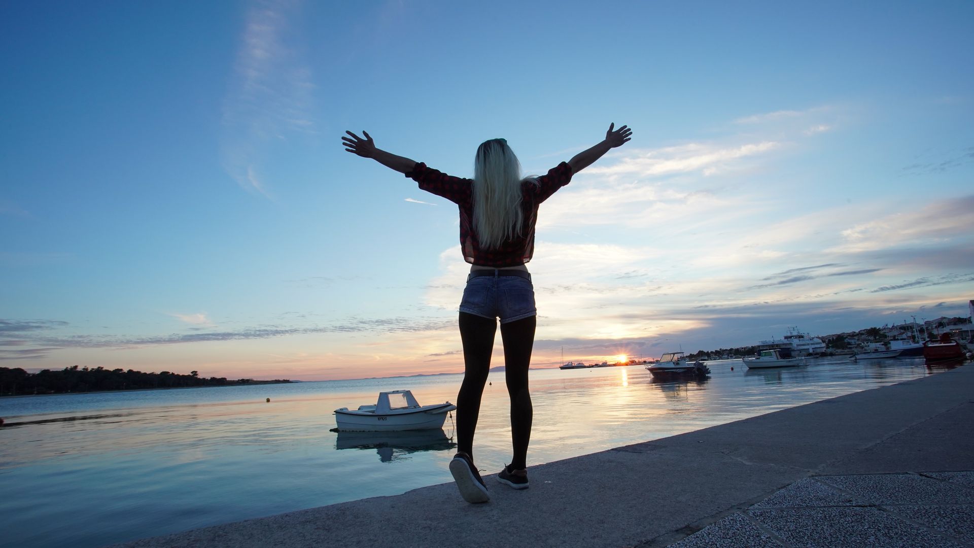 A girl with open arms at sunset on the sea front in Novalja