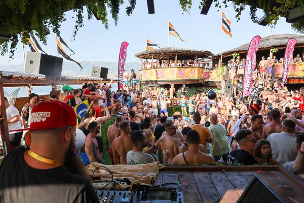 DJ at the decks in front of a sunny beach club crowd