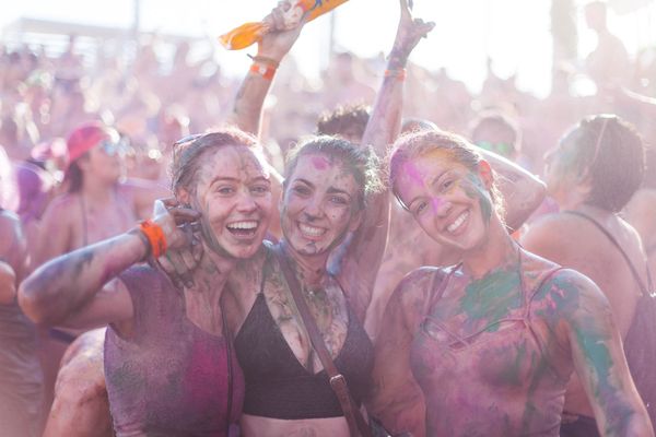 Three friends covered in colour powder, smiling